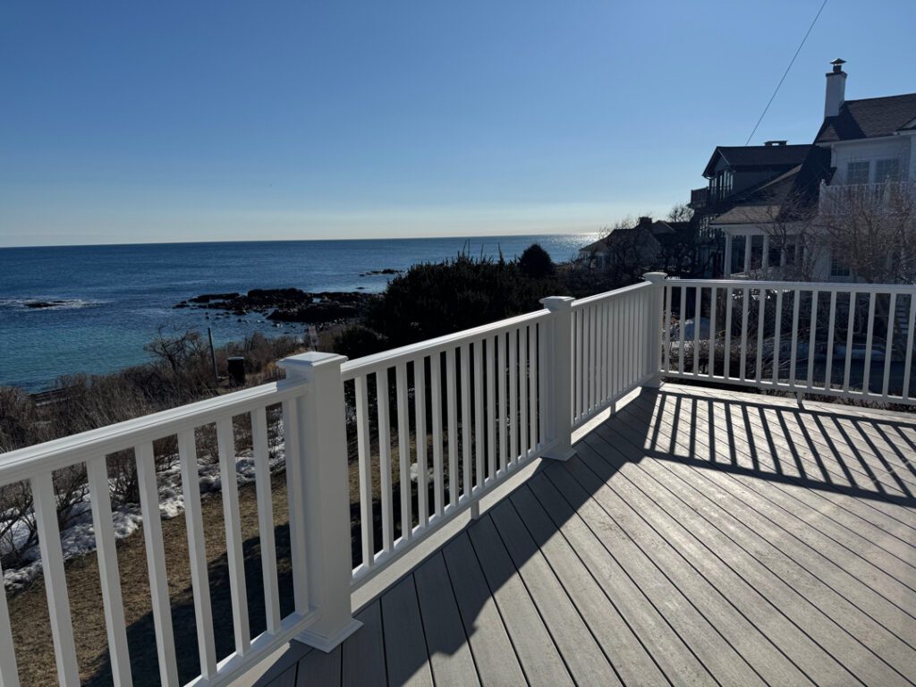 A custom ocean front deck utilizing a weathered grey composite decking and white railings to maintain the classic New England style